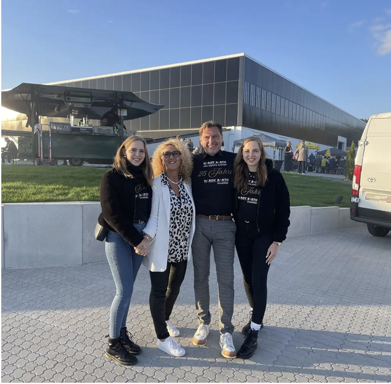 Hardy-Barth-Teammitglieder in 25-Jahre-Jubiläumsshirts vor der Firmenzentrale mit Photovoltaik-Fassade