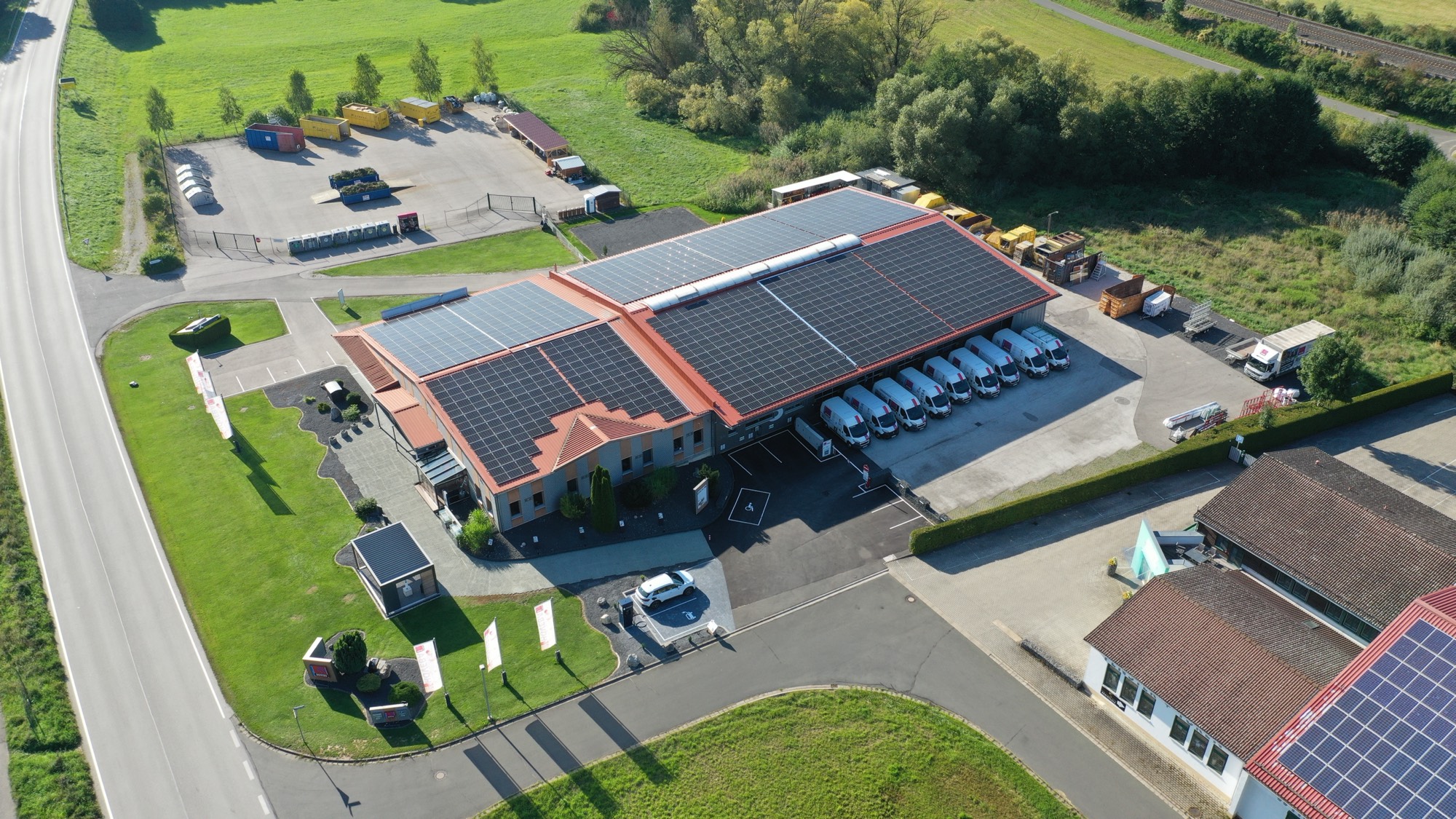 Luftaufnahme eines Firmengeländes mit Photovoltaik-Großanlage auf Dach und Carports in bayerischer Landschaft